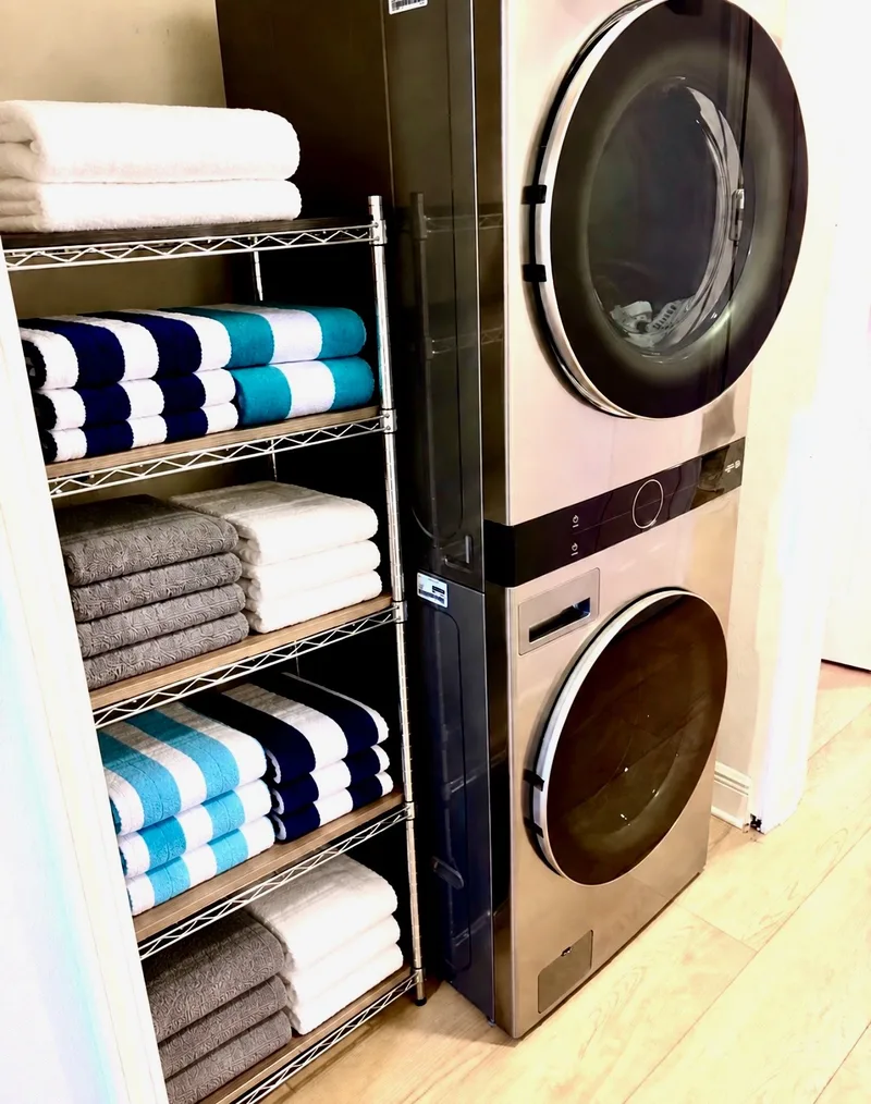 Stacked washer and dryer beside shelves of beach towels